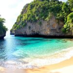 Pantai tersembunyi Bali dengan air jernih dan tebing hijau.